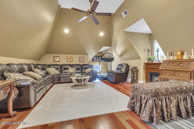 living area featuring visible vents, lofted ceiling, a glass covered fireplace, and wood finished floors