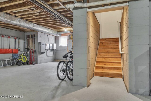 basement with electric panel, stairway, and concrete block wall