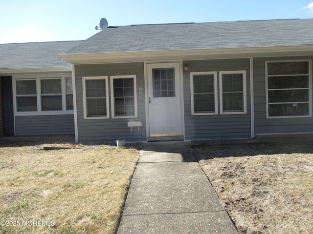 property entrance with a porch, a lawn, and roof with shingles