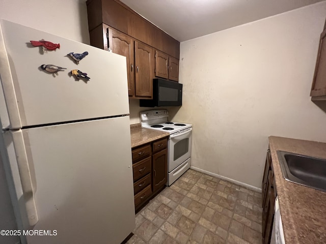 kitchen with white appliances, baseboards, stone finish flooring, dark brown cabinets, and a sink