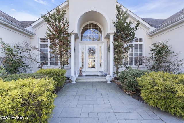 property entrance with roof with shingles and stucco siding