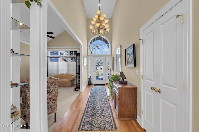 foyer entrance with baseboards, high vaulted ceiling, light wood finished floors, and an inviting chandelier