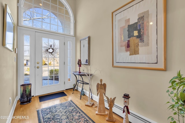 entrance foyer featuring a high ceiling, a baseboard radiator, wood finished floors, and baseboards