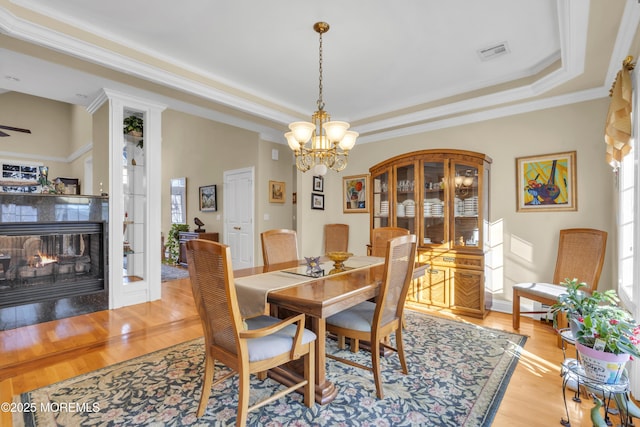 dining space featuring a raised ceiling, visible vents, light wood-style flooring, and a multi sided fireplace