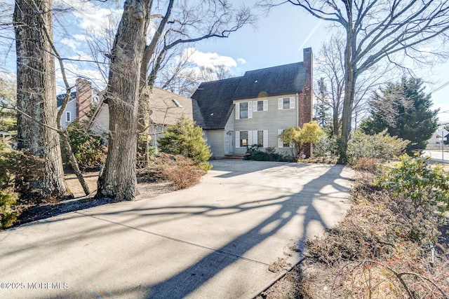 view of front of property with driveway, a chimney, and roof with shingles