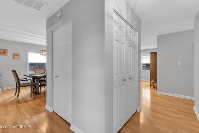 hall with visible vents, light wood-style flooring, and baseboards