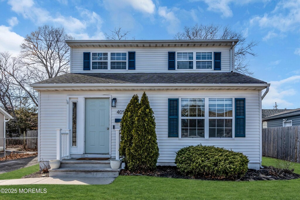 view of front of property featuring a shingled roof, fence, and a front lawn