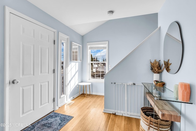 foyer with wood-type flooring, visible vents, vaulted ceiling, and baseboards