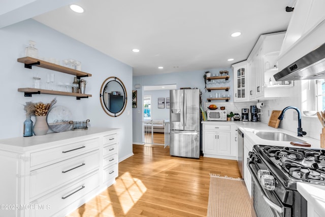 kitchen featuring appliances with stainless steel finishes, range hood, light wood-type flooring, open shelves, and a sink