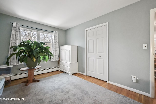 interior space with a baseboard heating unit, baseboards, and wood finished floors