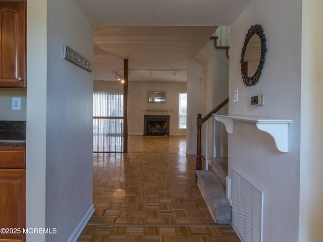 corridor with stairway, baseboards, visible vents, and rail lighting