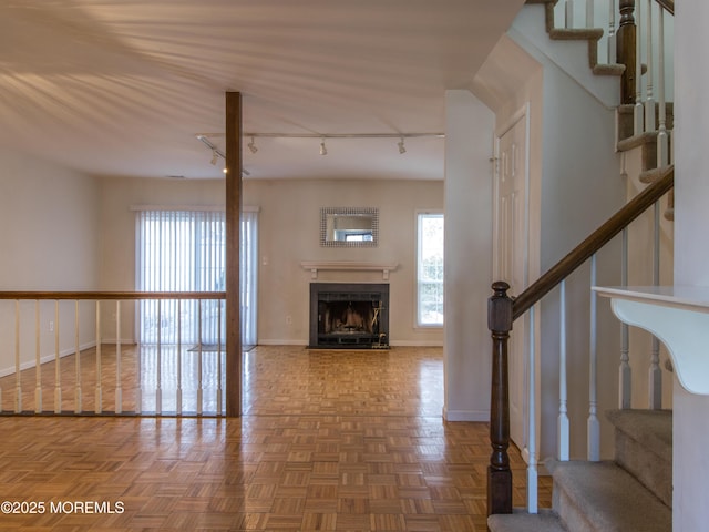 unfurnished living room featuring a fireplace with flush hearth, rail lighting, baseboards, and stairs