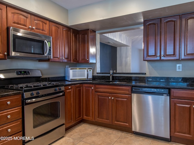 kitchen featuring stainless steel appliances, dark stone counters, a sink, and light tile patterned floors