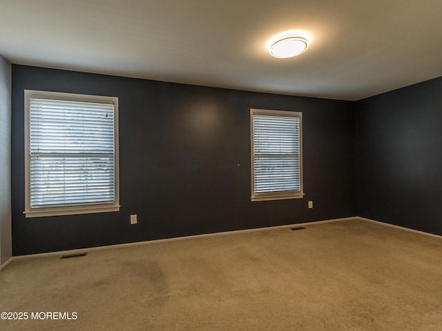 empty room with carpet, visible vents, and baseboards