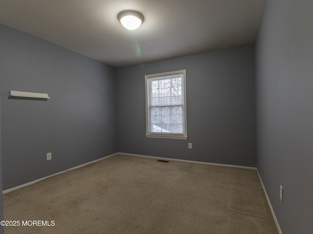 spare room featuring carpet floors, visible vents, and baseboards