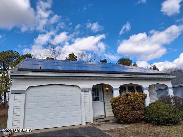 single story home featuring a garage, aphalt driveway, a porch, and solar panels