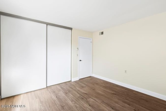 unfurnished bedroom with a closet, wood finished floors, visible vents, and baseboards