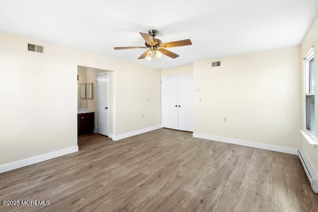 unfurnished bedroom with a baseboard radiator, visible vents, baseboards, and wood finished floors