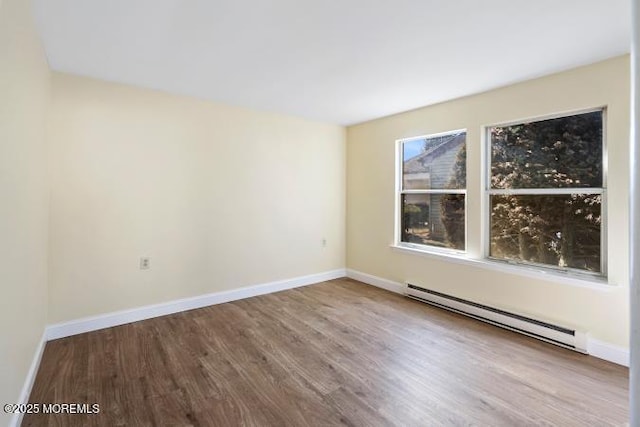 unfurnished room featuring a baseboard heating unit, wood finished floors, and baseboards