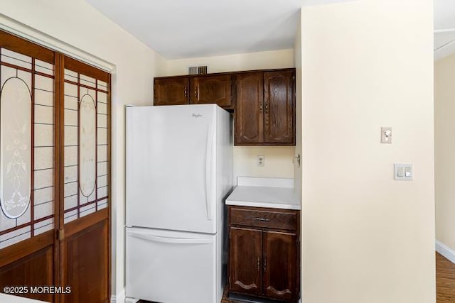 kitchen featuring dark brown cabinetry, visible vents, baseboards, light countertops, and freestanding refrigerator