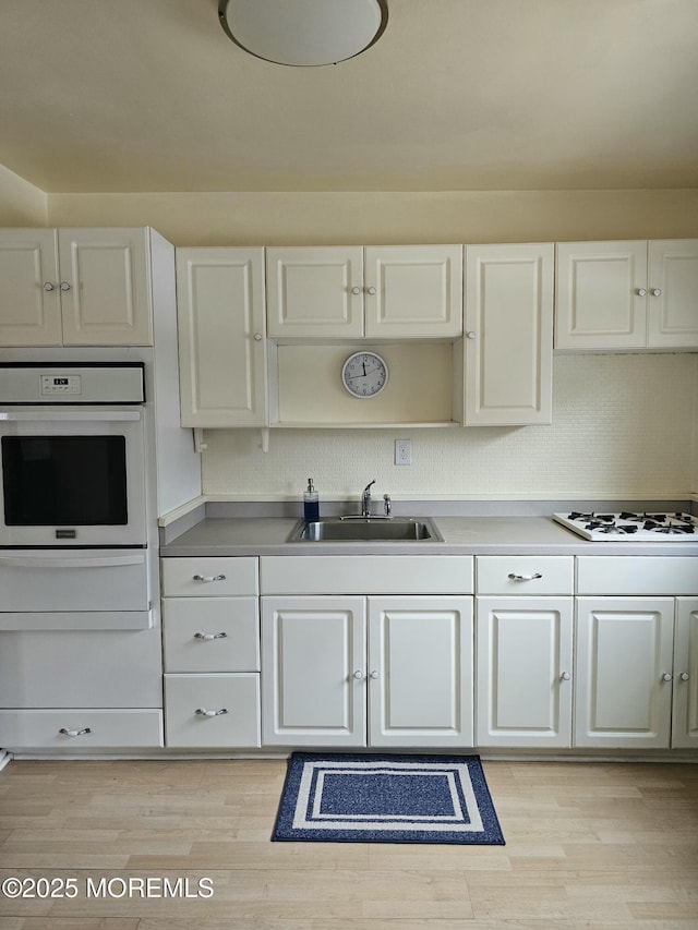 kitchen featuring white appliances, white cabinetry, light wood-style floors, and a sink