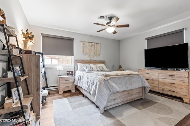 bedroom featuring light wood-style floors, baseboard heating, and a ceiling fan