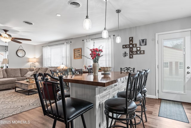 kitchen with wood finished floors, a kitchen bar, visible vents, and pendant lighting