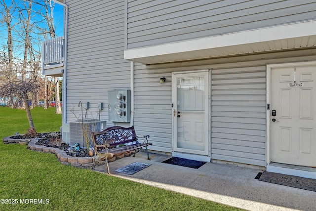 view of exterior entry with a lawn, a balcony, and central AC unit