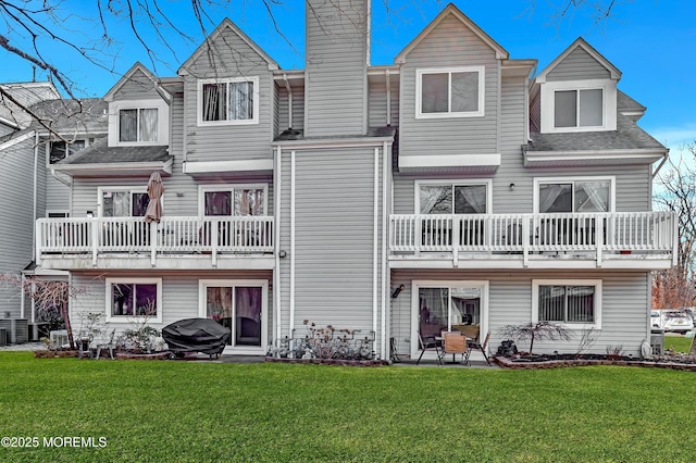 rear view of property with a balcony, a chimney, roof with shingles, a yard, and a patio area