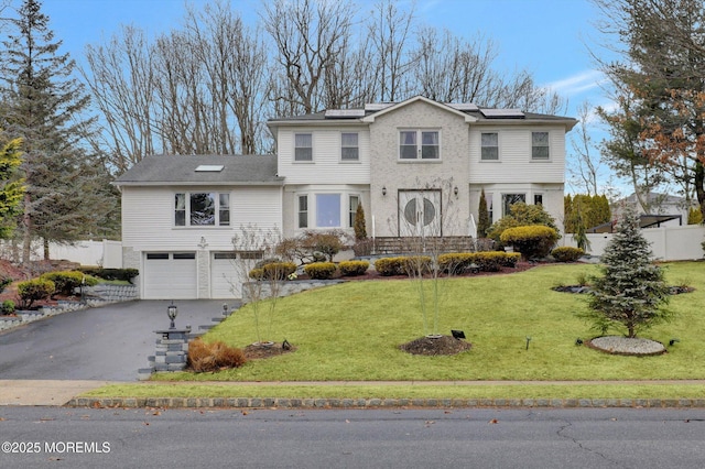 view of front of home featuring an attached garage, aphalt driveway, a front yard, and roof mounted solar panels