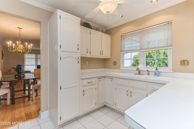 kitchen with light tile patterned floors, ornamental molding, a sink, light countertops, and white cabinets