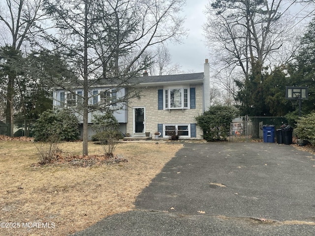 split foyer home featuring a chimney, entry steps, fence, stone siding, and driveway