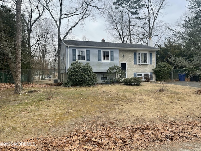 split foyer home with central AC unit, a chimney, fence, and a front lawn