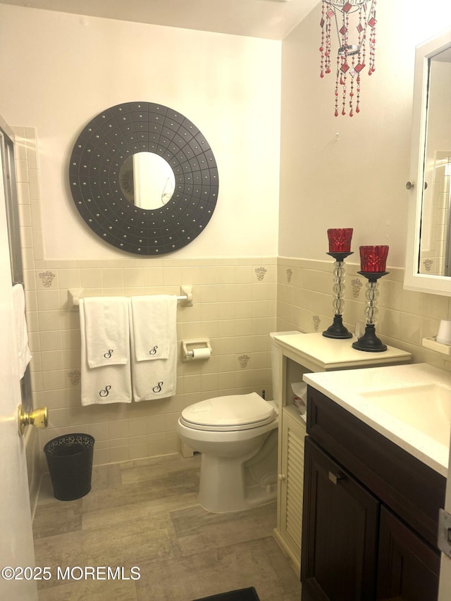 bathroom featuring toilet, wainscoting, vanity, and tile walls