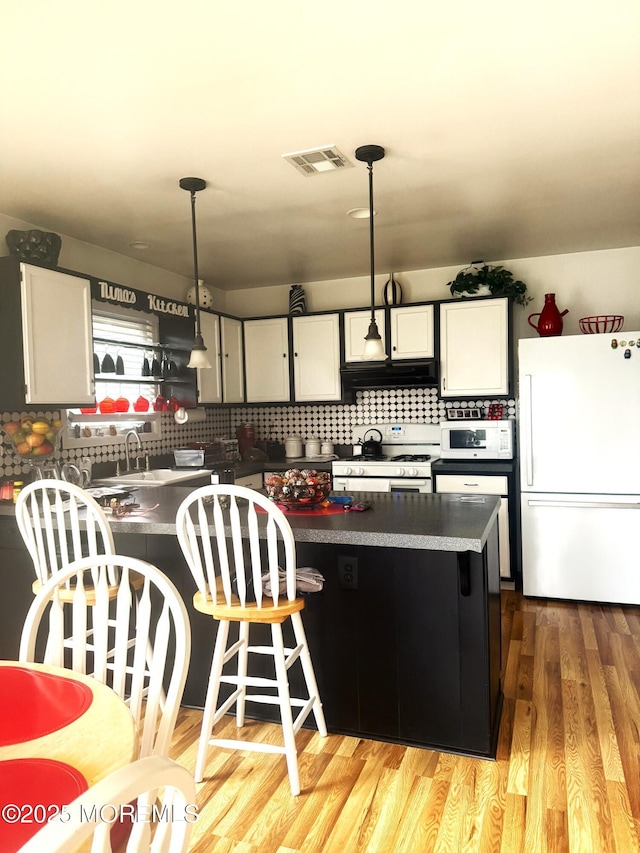 kitchen featuring a peninsula, white appliances, visible vents, light wood-style floors, and decorative backsplash