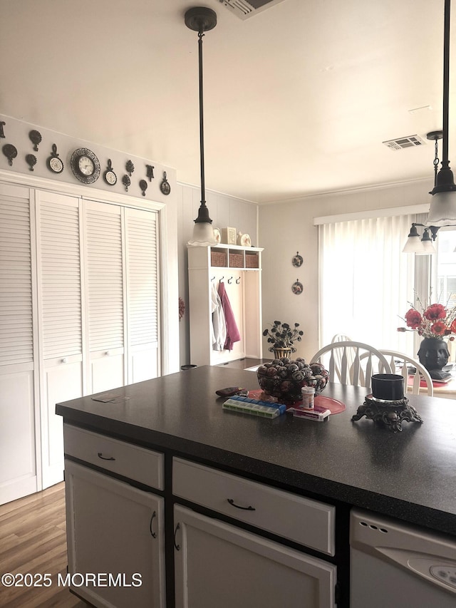 kitchen with white dishwasher, wood finished floors, visible vents, dark countertops, and pendant lighting