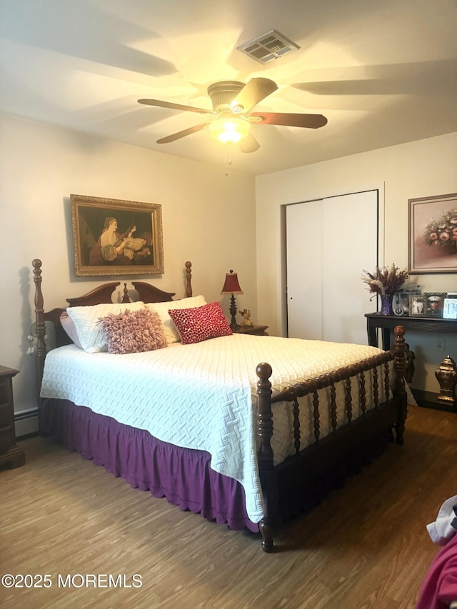 bedroom featuring ceiling fan, wood finished floors, visible vents, a closet, and baseboard heating