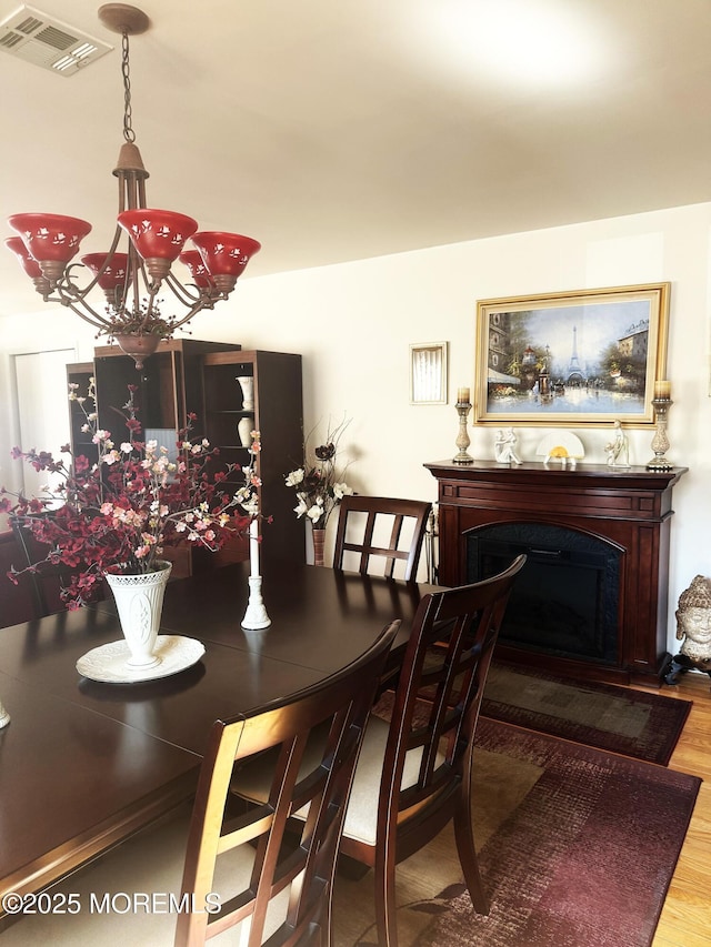 dining area featuring an inviting chandelier, a fireplace, visible vents, and wood finished floors