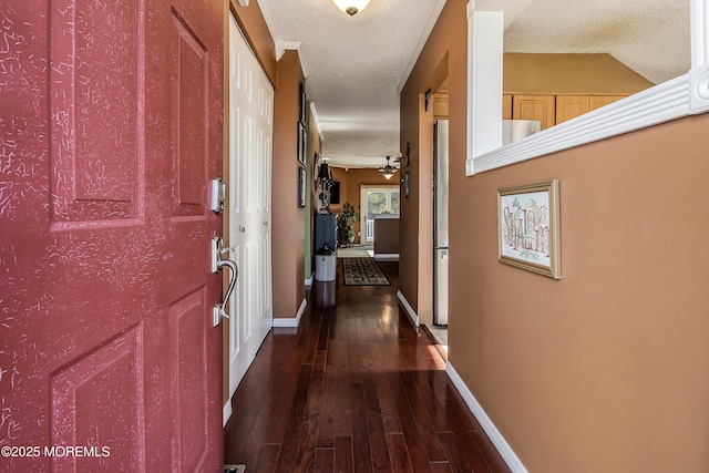 hallway featuring baseboards, dark wood finished floors, and a textured ceiling