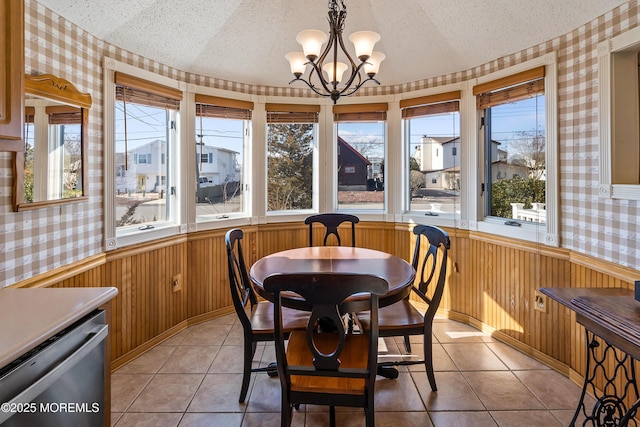 dining room featuring a chandelier, wainscoting, a textured ceiling, and wallpapered walls