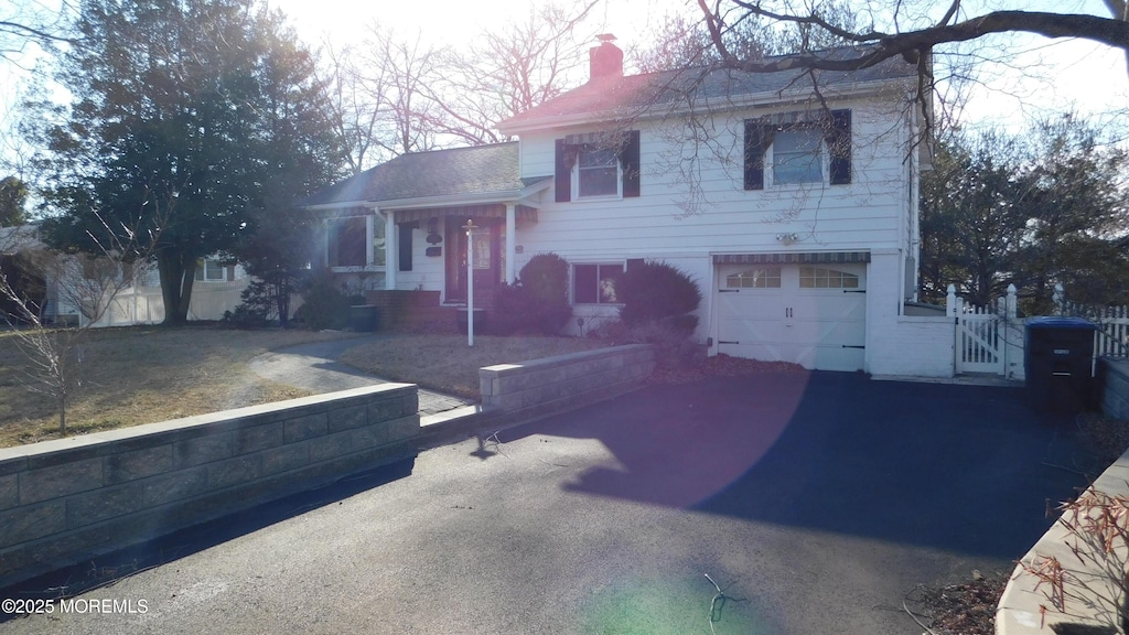 split level home with a garage, aphalt driveway, a chimney, and fence