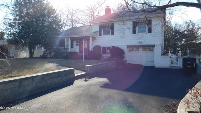 split level home with a garage, aphalt driveway, a chimney, and fence