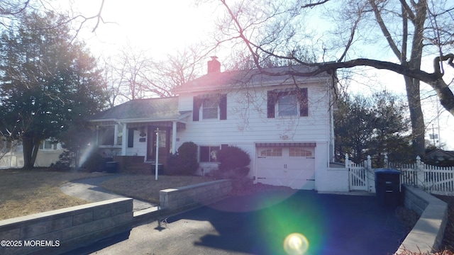 tri-level home featuring a garage, a chimney, fence, and a gate