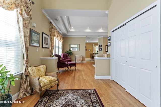 entryway featuring crown molding, a raised ceiling, light wood-style flooring, and baseboards