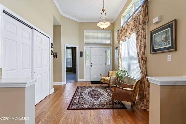 entrance foyer featuring a towering ceiling, light wood-style flooring, ornamental molding, and baseboards