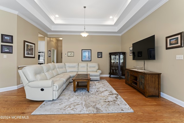 living area with baseboards, a tray ceiling, wood finished floors, and ornamental molding