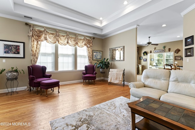 living area with a raised ceiling, crown molding, and wood finished floors