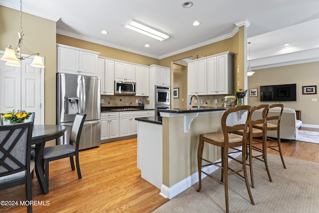 kitchen with dark countertops, a peninsula, stainless steel appliances, crown molding, and light wood-type flooring