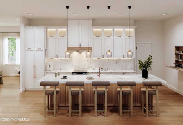 kitchen featuring light stone counters, a center island with sink, light wood finished floors, decorative backsplash, and white cabinets