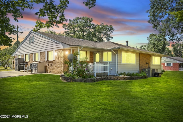 view of front facade featuring driveway, fence, central AC unit, and a front lawn